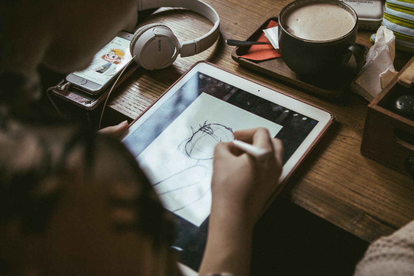 Umelec kreslí na digitálny tablet pri drevenom stole.